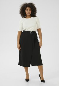 Haut blanc à manches courtes associé à une jupe enveloppante noire, avec une ceinture à boucle circulaire. La jupe a une texture lisse et un design jusqu'aux genoux.