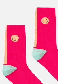 Calcetines rosa con canalé y diseño de cara sonriente en naranja en el puño, complementados con detalles en azul claro en la punta y el talón.