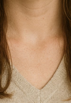 Gros plan sur le cou et le haut de la poitrine d'une personne à la peau claire, portant un pull beige à col en V en maille, avec des cheveux bruns tombant de chaque côté.