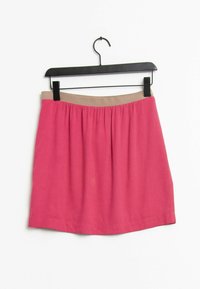 Jupe en tissu rose avec une taille élastique beige, présentant une texture froncée et un ourlet droit, accrochée sur un cintre noir contre un fond blanc.
