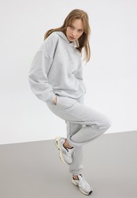 Grå hoodie och joggers i mjukt tyg. Outfiten har en avslappnad passform, med ribbade cuffs och sidofickor. Bärs med träningsskor.