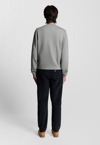 Grå sweatshirt i borstad tyg med långa ärmar, kombinerad med mörkblå byxor. Har detaljer med gult logotyptryck på bakfickan.