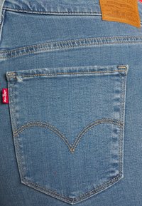 Denimjeans baglomme i lyseblå med en karakteristisk buet broderi i guldtråd. Rødt Levi’s-mærke synligt på venstre side.