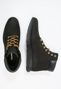 Stivaletti neri in suede con lacci gialli e occhielli dorati, dotati di suola in gomma e dettagli in pelle. Finitura testurizzata con design alto.