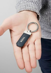 Juodas odinis raktų pakabukas su sidabrinėmis detalėmis, turintis stačiakampį žymeklį su įspaustu užrašu "BOSS." tekstūruotas paviršius, šešiakampė forma.
