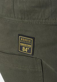 Olive green fabric with a smooth texture, featuring a black and yellow rectangular tag that reads "NORDIC WOODLANDS VANDERSTORM 84°."