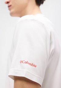 Λευκό κοντομάνικο t-shirt από βαμβάκι, με κόκκινο λογότυπο "Columbia" στο αριστερό μανίκι. Λείος υφής και κλασικός σχεδιασμός.