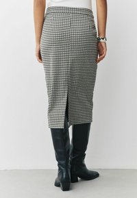 Svartvit houndstooth kjol med en slits bak, skräddarsydd passform, bärs med knähöga svarta läderstövlar. Slät textur, strukturerad design.