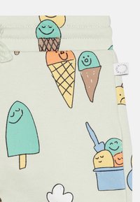 Jasnozielone spodnie dresowe z kolorowymi ilustracjami lodów, w tym rożków i lodów na patyku, z wesołymi buźkami i prostymi konturami.