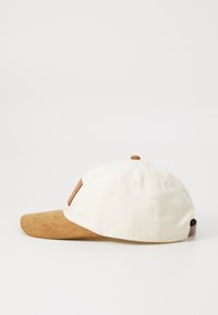 Cepure ar baltu kokvilnas auduma korpusu un brūnu zamšādu malā. Iespēja ādas plāksne priekšā un tradicionālas ventilācijas atveres.