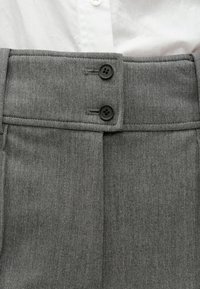 Hallid kohandatud püksid kahe suure musta nupuga kõrgel vöökohal. Valmistatud tekstuurse kangaga, esiküljel laskudega lisadetailiks.