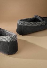 Mustat mokkashuovat, joissa on harmaa kudottu kangasranneke ja pehmeä sisäpinta, joissa on pyöreä muoto ja matala profiili.
