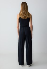 Tutina nera con top aderente e design a gamba larga, realizzata in tessuto liscio. Presenta una vita elastica e fessure laterali vicino all'orlo.