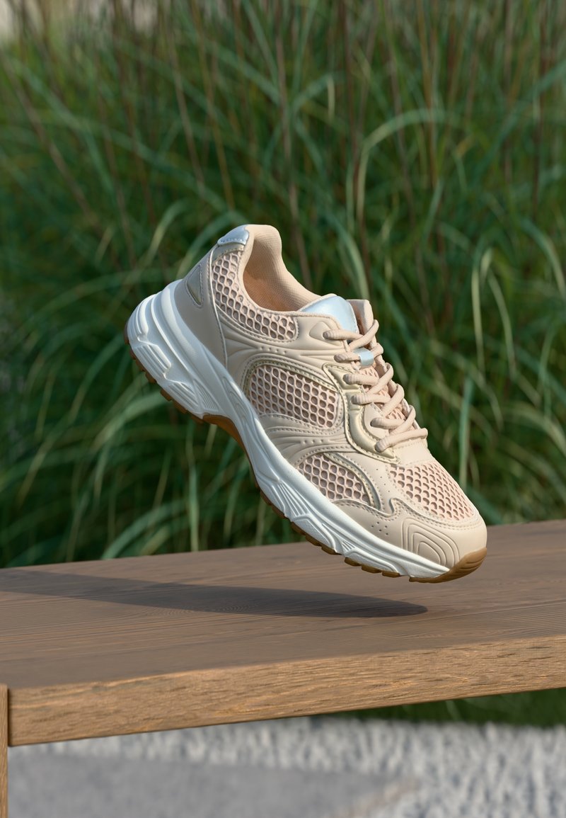 Chaussure de sport beige avec une tige en mesh, semelle en caoutchouc et col rembourré. Présente des accents texturés et une fermeture à lacets.