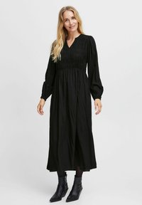 Svart maxiklänning med smockad bodice, långa puffärmar och V-ringning. Styleras med ankelstövlar, har en avslappnad passform och textil med struktur.