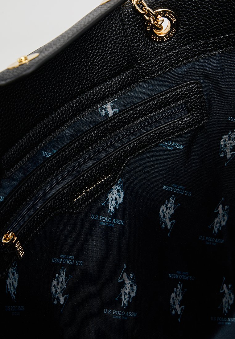 Intérieur de sac à main texturé noir avec un compartiment zippé ; doublure décorée d'un motif répété du logo U.S. Polo Assn. en bleu.