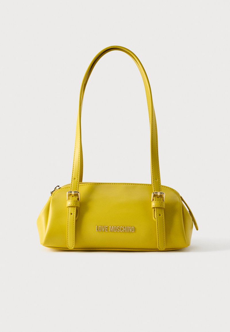 Κίτρινη τσάντα χειρός από συνθετικό δέρμα με δύο λουριά για τον ώμο, ορθογώνιο σχήμα, επιχρυσωμένες μεταλλικές λεπτομέρειες και ανάγλυφο λογότυπο στο μπροστινό μέρος.