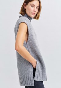 Grau gestrickter ärmelloser Rollkragenpullover mit seitlichen Schlitzen und geripptem Saum. Das strukturierte Material zeigt subtile Variationen im Garn.