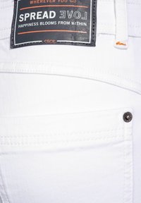 Witte denim jeans met een gestikte achterzak, metalen knop en een zwart label met witte tekst op de tailleband.
