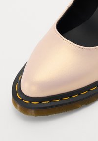 Scarpa in pelle rosa chiaro con punta affusolata, suola in gomma nera e cucitura gialla lungo il bordo. Texture liscia con design elegante.