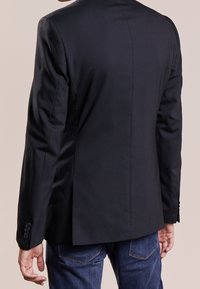 Svart blazer med skräddarsydd passform, enkel springa bak och knäppta manschetter. I kombination med blå denimjeans. Slät, vävd textur.