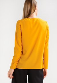 Dlouhý rukáv top v živé žluté barvě, vyrobený z hladké tkaniny. Jednoduchý design s kulatým výstřihem a rovným zadním lemem.