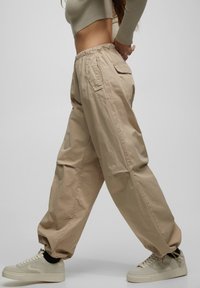 Beige cargobroek met een elastische tailleband, zijzakken en een taps toelopend ontwerp, gecombineerd met lichte sneakers en een aangesloten top.