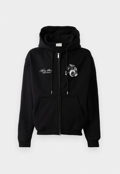 Μαύρη ζακέτα με φερμουάρ και κορδόνια, με λευκή κείμενη επιγραφή "Filling Piece United By Rhythm" και γραφικό με σύνολο τρομπέτας στην περιοχή του στήθους.