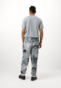 Szürke póló, rövid ujjakkal, puha, polár nadrággal, amely szürke és fekete álcázott mintázatú. Fekete cipő egészíti ki a megjelenést.