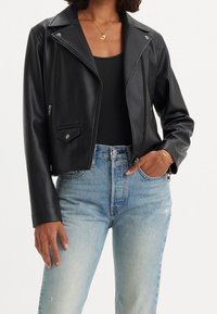 Czarna kurtka motocyklowa z czarnej sztucznej skóry o krótkim kroju, z srebrnymi elementami, ukośnym zamkiem błyskawicznym i kieszenią zapinaną na zatrzask.