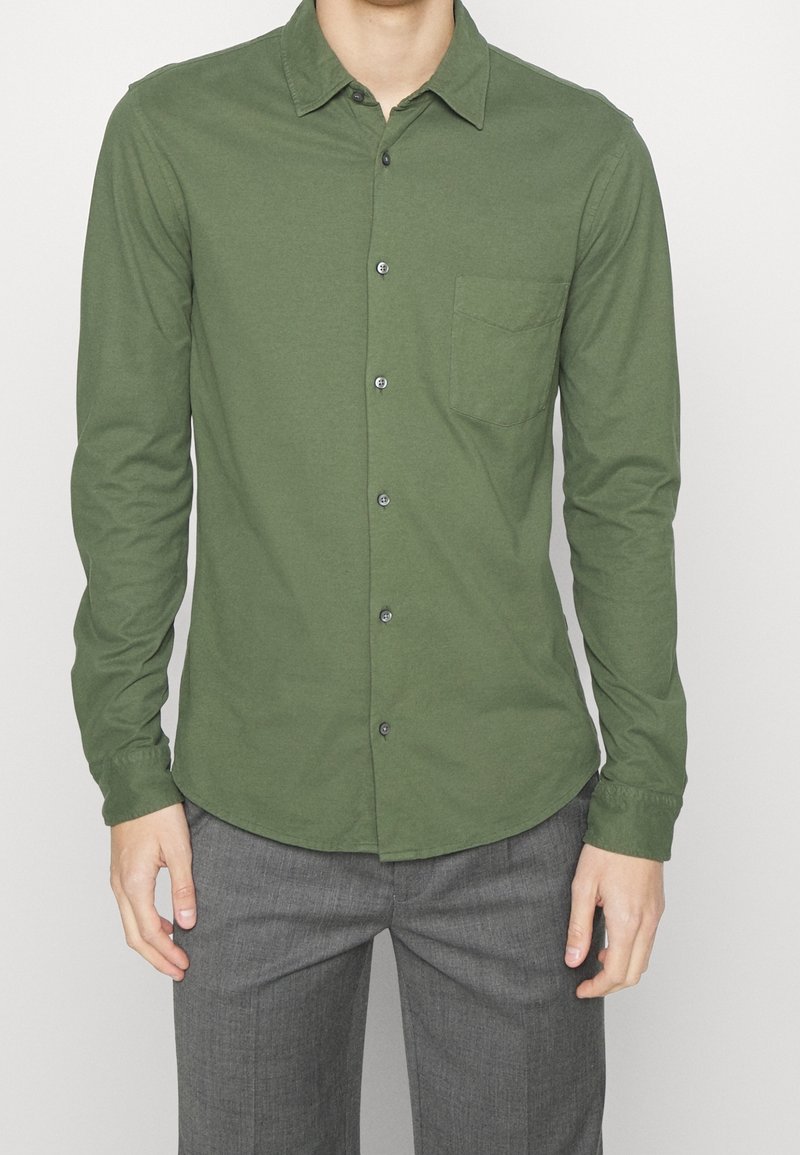 Zelená košile s dlouhým rukávem a knoflíky vyrobená z měkké tkaniny, obsahující kapsu na prsou, špičatý límec a tmavé knoflíky.