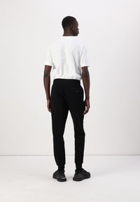 Zwarte joggers met een aansluitend ontwerp, geribbelde manchetten en een achterzakaccent, gecombineerd met een eenvoudig wit T-shirt met korte mouwen.