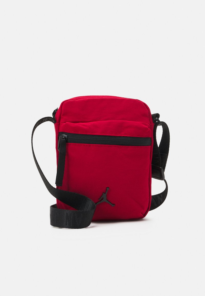 Rød stof crossbody taske med sorte detaljer, der har en front lynlås lomme og justerbar rem. Broderet logo på fronten.