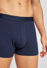 Marineblaue Baumwoll-Boxerbriefs mit einem weichen elastischen Bund, ausgestattet mit einer Vorderpouch und flachen Nähten für zusätzlichen Komfort, gezeigt auf einem Oberkörper.