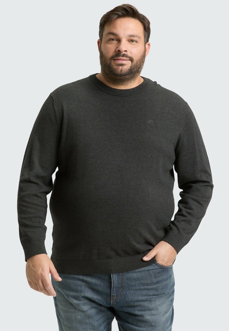 Donkergrijze trui van zachte stof, met een ronde halslijn en geribde manchetten. Gedragen met blauwe jeans, subtiele logo-details zichtbaar.