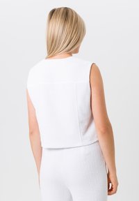 Witte, mouwloze top gemaakt van gestructureerde stof met een cropped ontwerp. Heeft een gladde halslijn en een achternaaddetail.