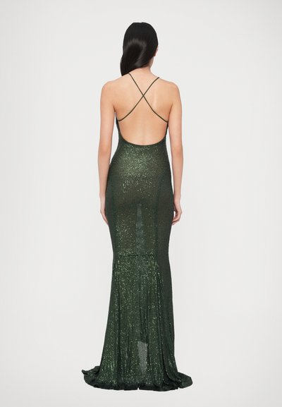 Tamsiai žalia aptempianti suknelė su blizgančia tekstūra, žemu atviru nugaros kirpimu ir susikryžiavusiomis petnešėlėmis, apačioje išsišakojanti.