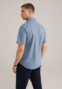 Īsas piedurknes, gaiši zila krekls, izgatavots no mīksta auduma, ar norādītu jostu, aizmugurējo apkakli un izliekumu apakšmalā. Nēsāts ar tumšām biksēm.