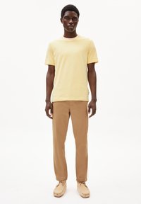 Hellgelbes, kurzärmliges T-Shirt kombiniert mit sandfarbenen Hosen und beigen Mokassins. Einfaches, lässiges Design, glatte Textur.