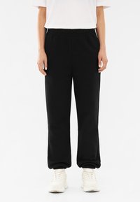 Zwarte sweatpants met een elastische tailleband, taps toelopende pijpen en een gladde textuur, gecombineerd met witte sneakers. Eenvoudig, minimalistisch ontwerp.