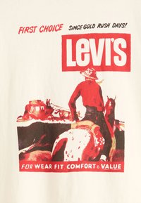 Witte T-shirt met rode grafische print. Bevat een cowboy op een paard met het "Levi's" logo en slogan, retro stijl met vetgedrukte tekst en kleuren.