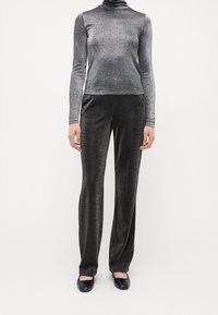 Metallic silberner Rollkragenpullover kombiniert mit glänzenden schwarzen weiten Hosen. Beide Kleidungsstücke haben eine glatte Textur und einen subtilen Schimmer. Schwarze flache Schuhe.