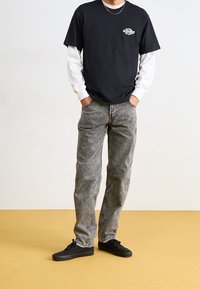 T-shirt noir superposé à un haut à manches longues blanc, associé à un jean gris déchiré et des baskets noires. Design simple, coupe décontractée.