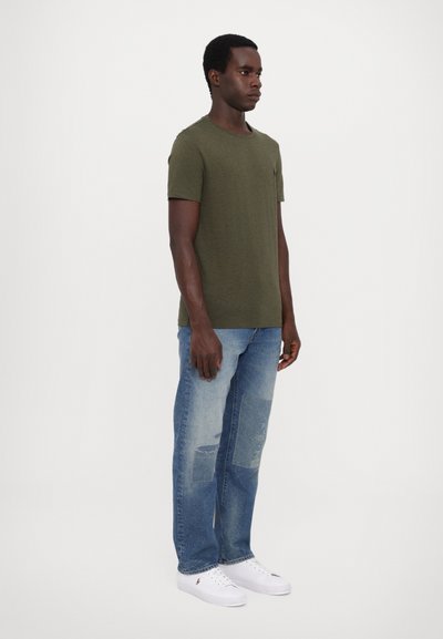 Olivgrön t-shirt med kort ärm, kombinerad med ljusblå slitna jeans och vita sneakers. Skjortan har en enkel design utan mönster.