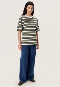 Camiseta a rayas olivas con cuello redondo blanco, combinada con pantalones de mezclilla anchos de color azul y zapatos marrón oscuro.