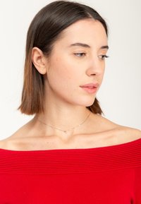 Top rojo sin hombros con textura acanalada, collar de plata con un pequeño colgante y cabello castaño lacio en un estilo natural.