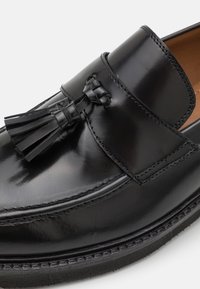 Zwarte leren loafers met een gladde afwerking, voorzien van een decoratieve kwast, gestikte accenten en een laag profiel rubberen zool.