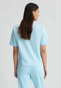 Top azzurro chiaro a maniche corte realizzato in tessuto morbido, con una vestibilità comoda e orli arrotolati. Sul retro presenta una texture liscia e cuciture minime.