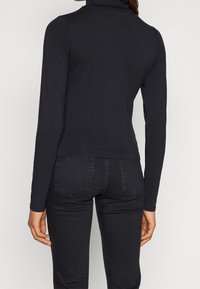 Black long-sleeve turtleneck top made from soft fabric, featuring a slim fit and seamless construction at the neckline, with no visible patterns.