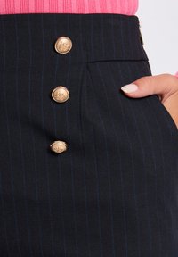 Jupe noire à rayures avec des boutons décoratifs dorés, en tissu lisse, taille haute et détails de poches sur le côté.